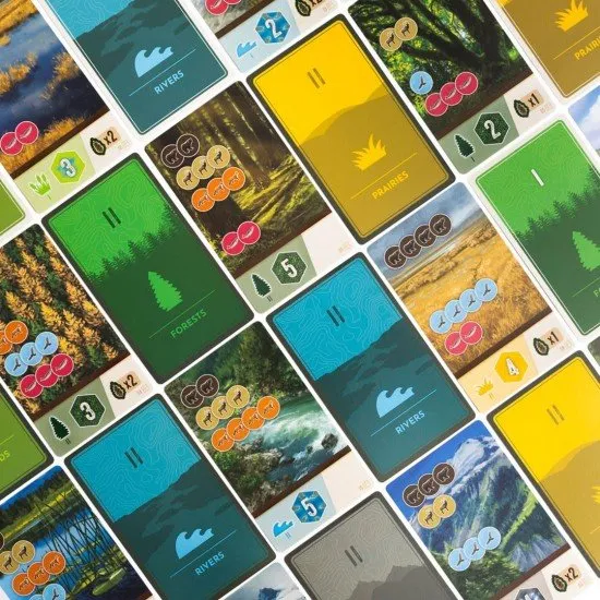 Colourful dice featuring animal icons alongside illustrated habitat sheets and cards depicting the rolling hills of Cascadia