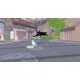 A small black cat wearing a green dinosaur hat sitting on a busy city pavement surrounded by tall buildings