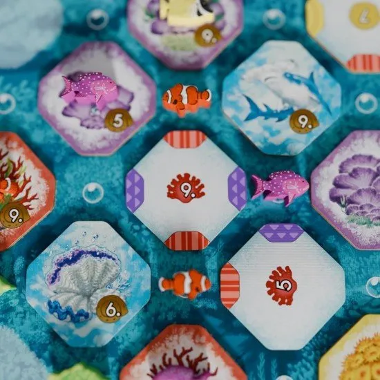 Colourful coral reef tiles and sea-life tokens arranged on a table to show a developing underwater habitat